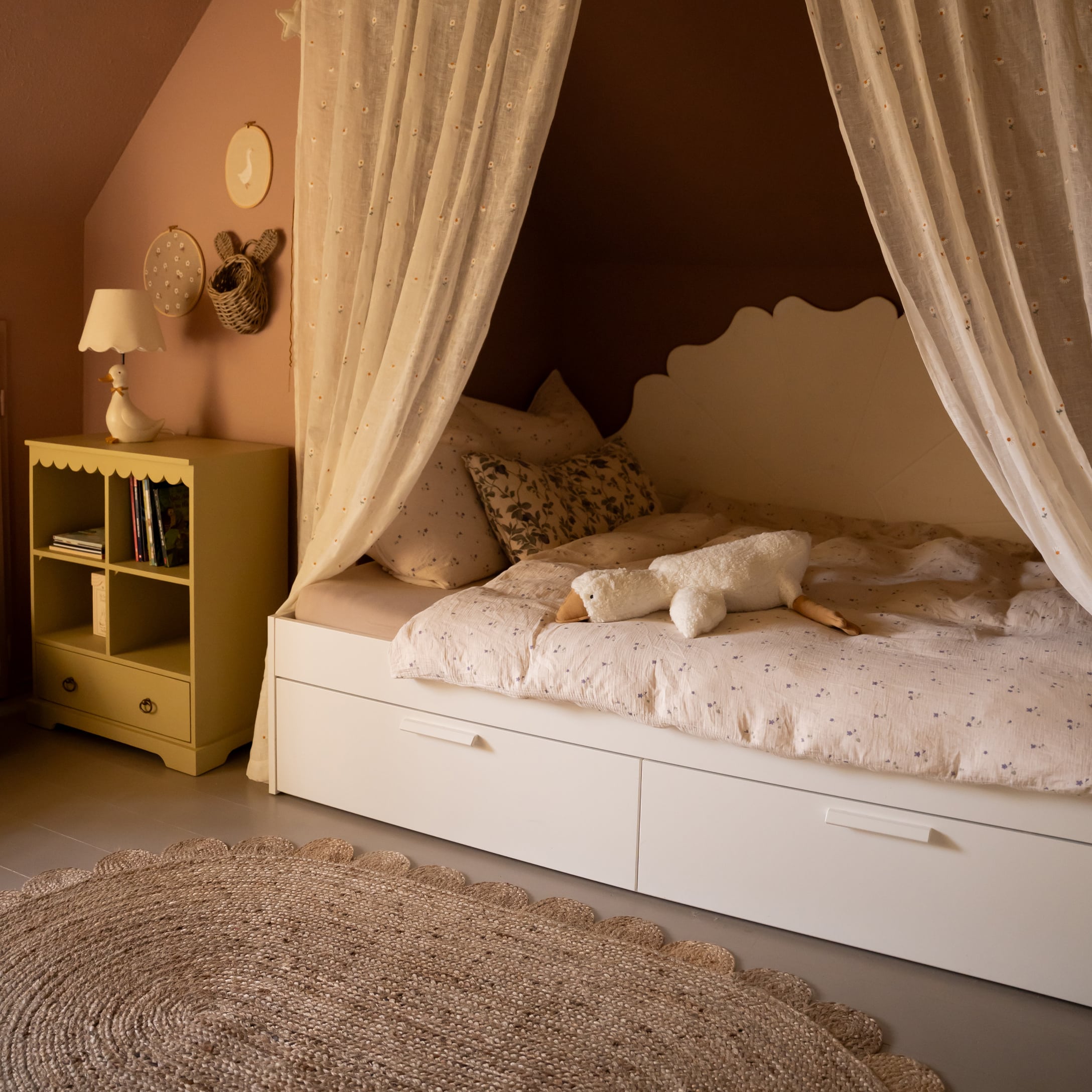 Gemütliches Kinderbett mit weissem Rahmen, Vorhängen und Plüschgans auf gemusterter Bettwäsche