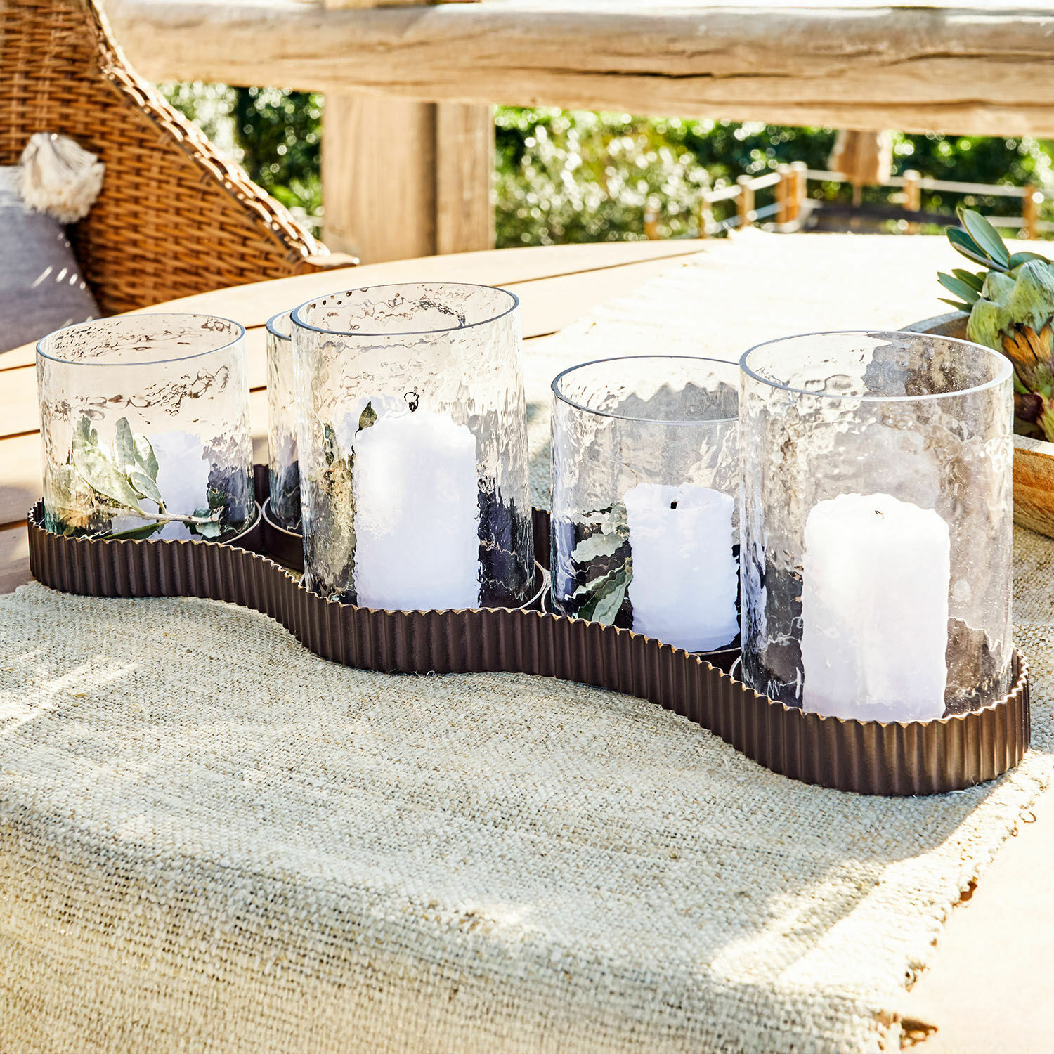 Windlicht Méridienn Set aus 5 Glaswindlichtern mit weissen Kerzen auf braunem Metallständer auf Gartentisch