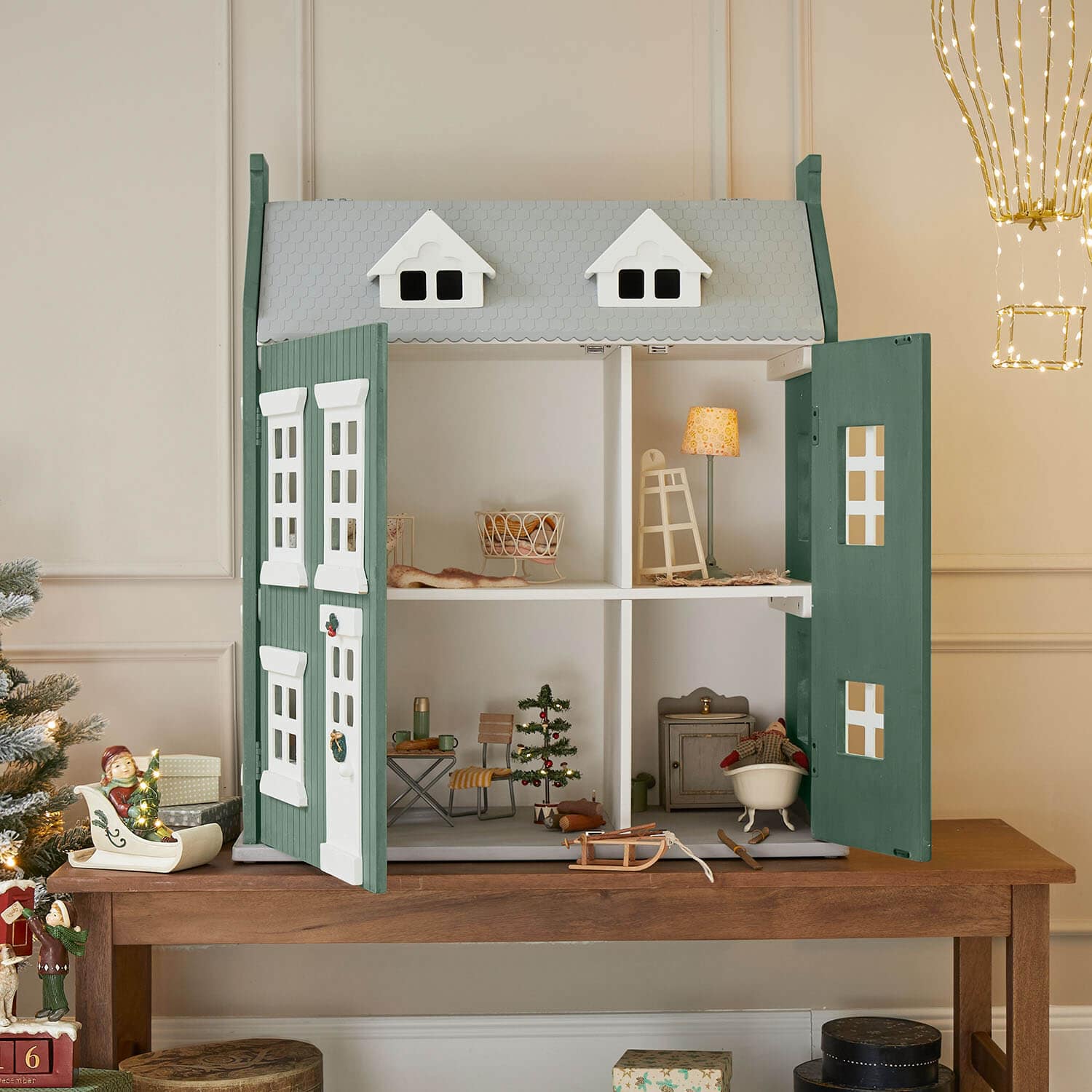 Grünes und graues Holz-Puppenhaus mit offenen Türen und weihnachtlicher Dekoration innen
