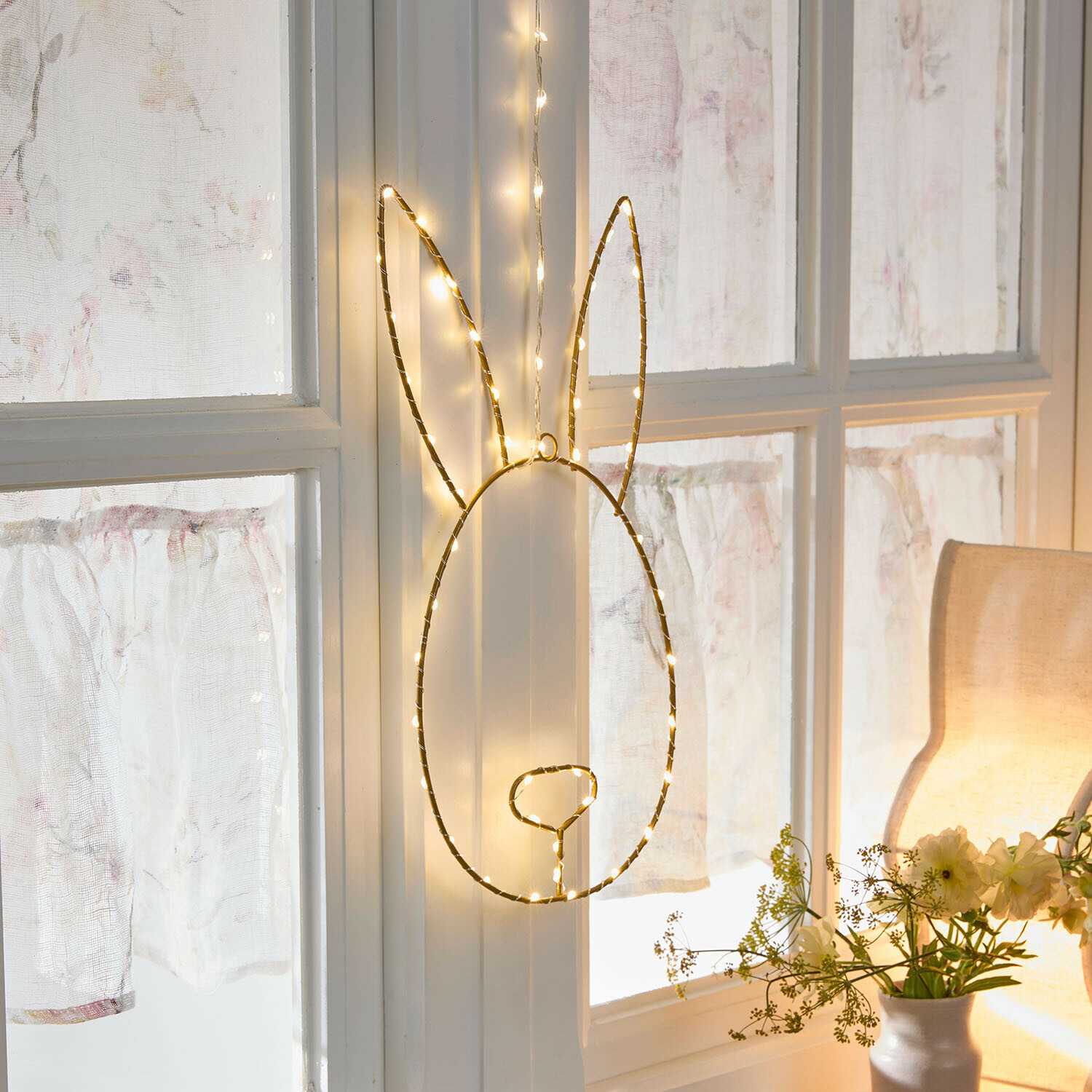 LED-Dekoration in Hasenform mit warmweißen Lichtern, hängend an weißem Fenster im Wohnzimmer