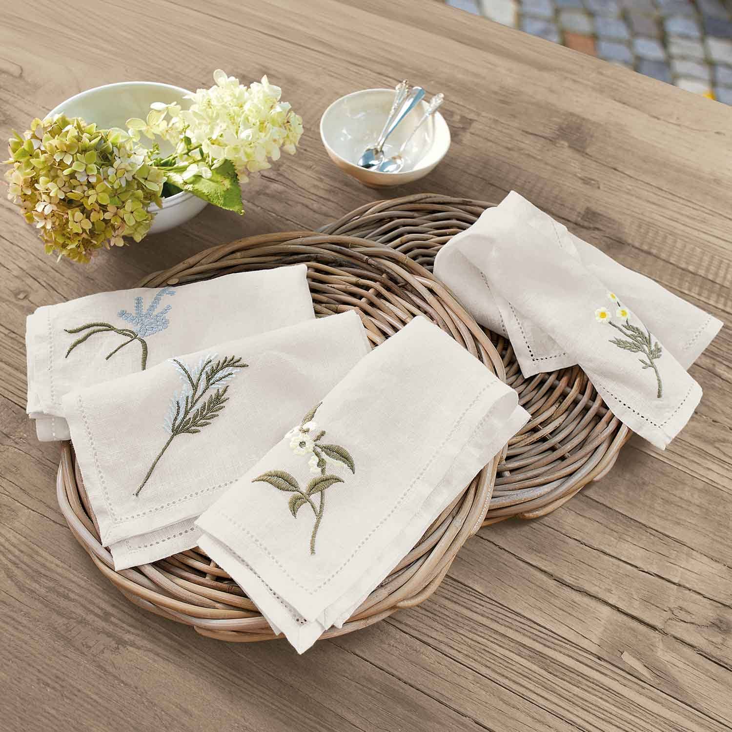 Leinenservietten in Creme mit Blumenstickerei auf Weidenkorb auf Holztisch