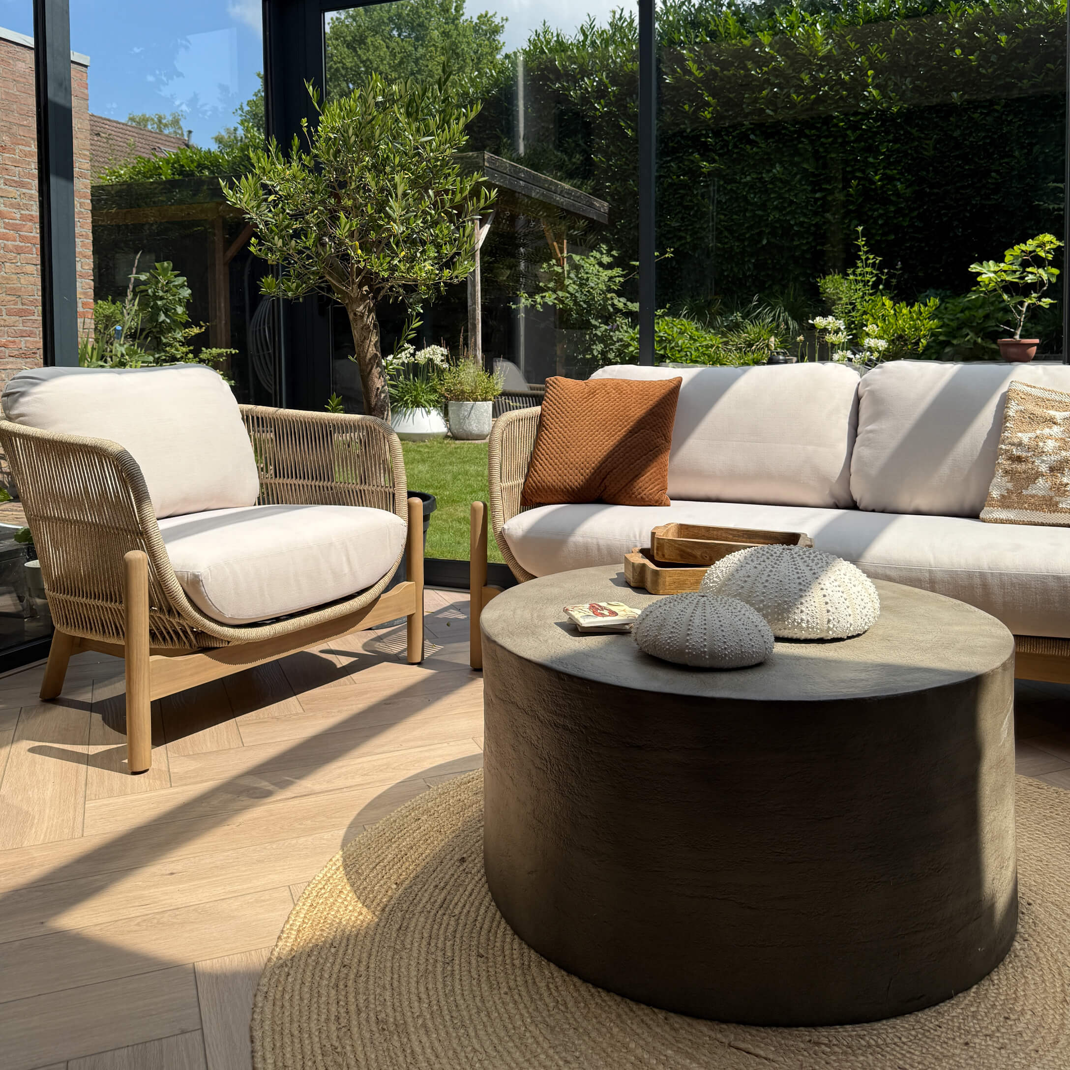 Moderner Wohnraum mit beigem Sofa, Holz- und Stoffsessel sowie rundem schwarzem Couchtisch