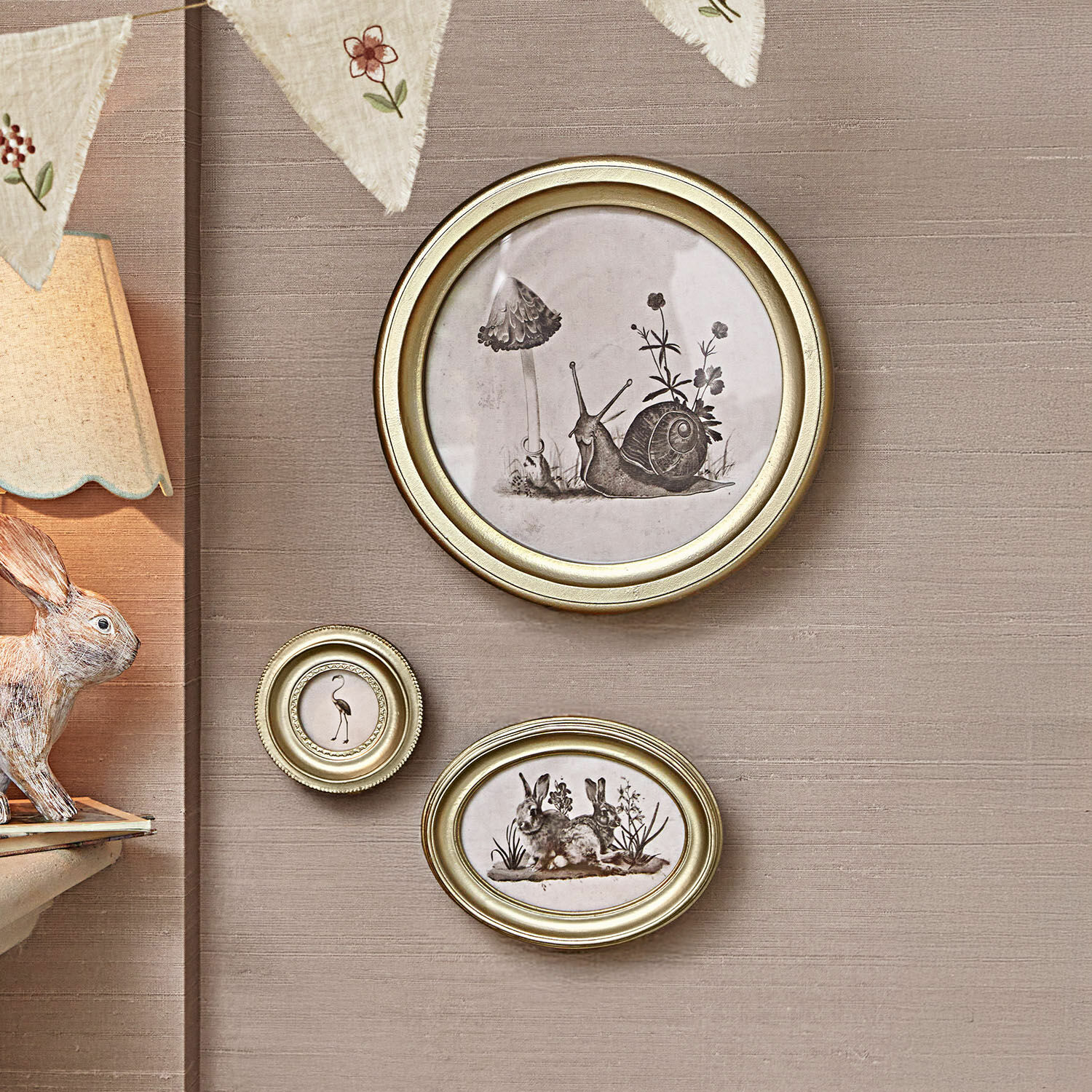 Bild 3er Set Atriana Drei goldene Bilderrahmen mit schwarz-weissen Tier- und Pflanzenillustrationen an beiger Wand.