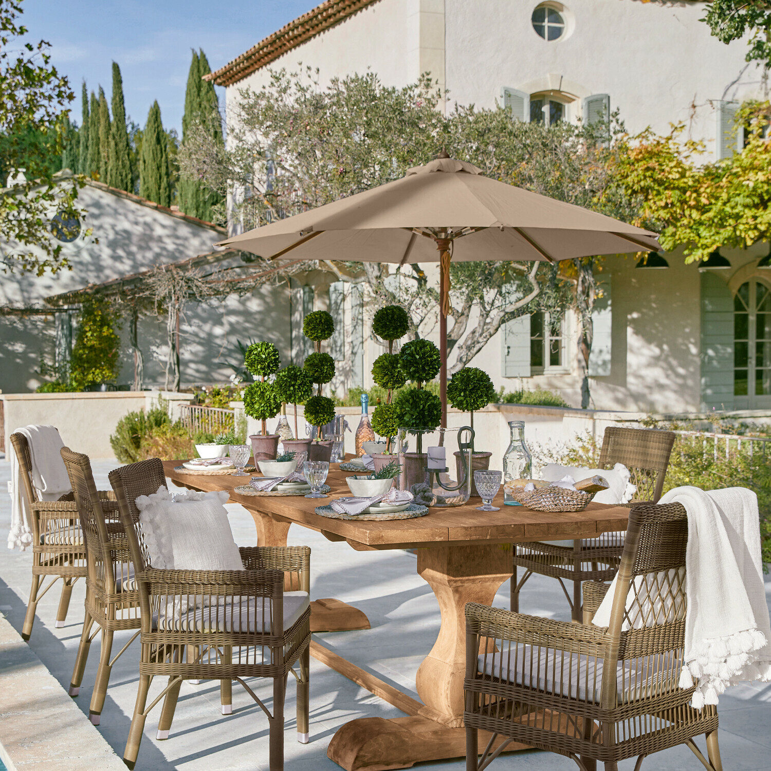 Sonnenschirm Brent Grosser Holzgarten-Tisch mit Rattanstühlen und beigem Sonnenschirm auf sonniger Terrasse