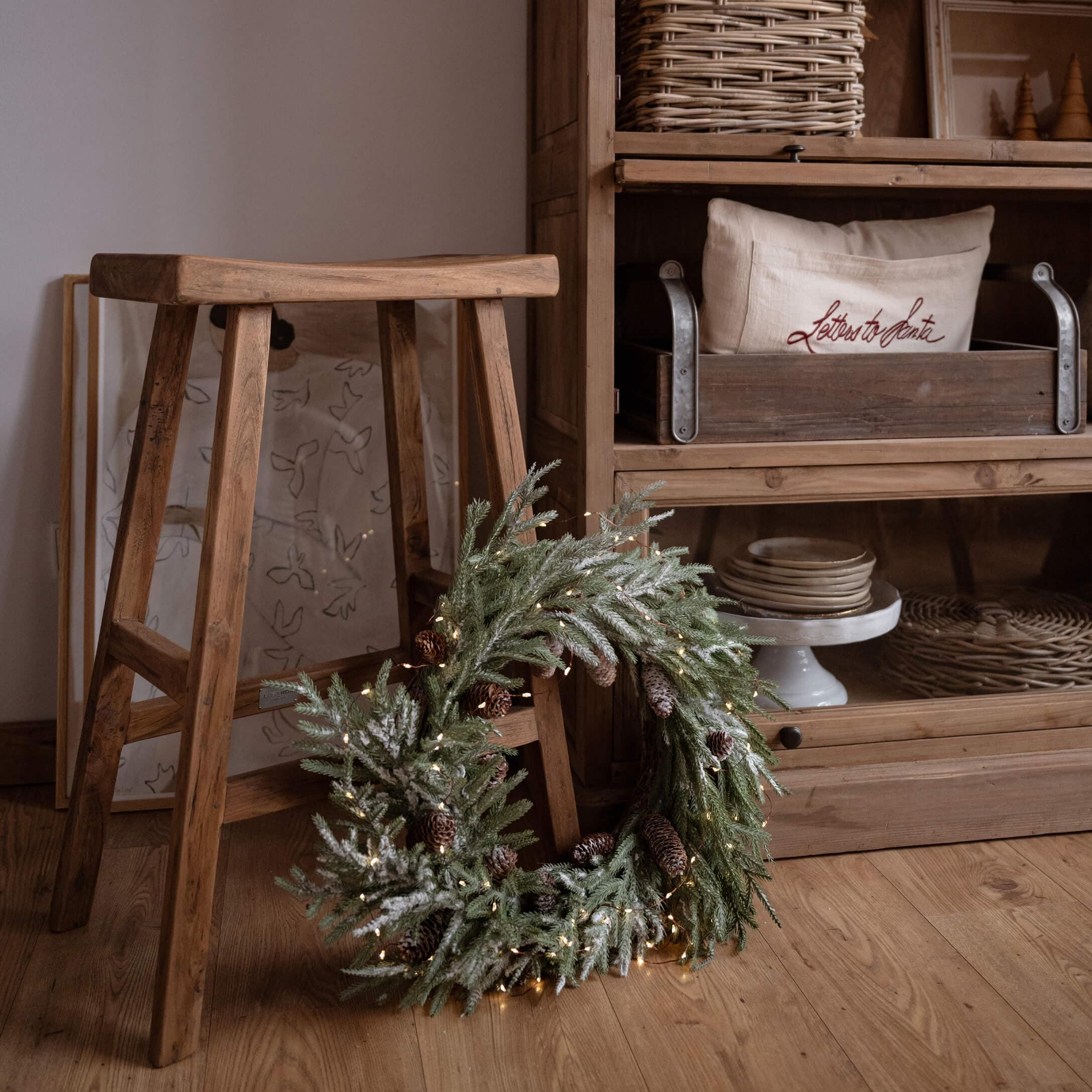 Weihnachtlicher Dekokranz mit grünen Zweigen und Zapfen auf Holzboden neben einem Holzschemel