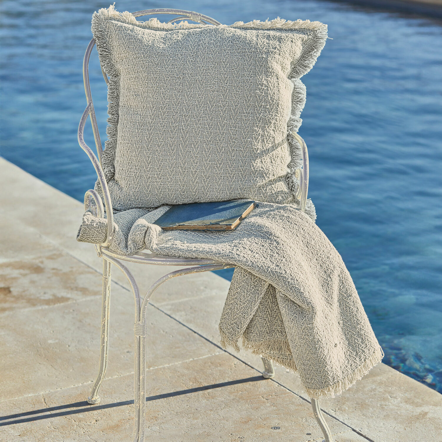 Beige Kissen und Fransen-Decke auf Metallstuhl am Wasser, Wohn- und Gartendekoration