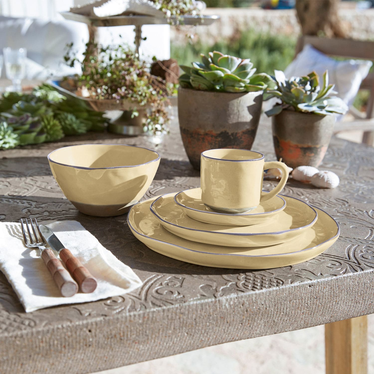 Keramik-Geschirrset in Creme mit blauem Rand auf rustikalem Tisch mit Sukkulenten-Dekoration