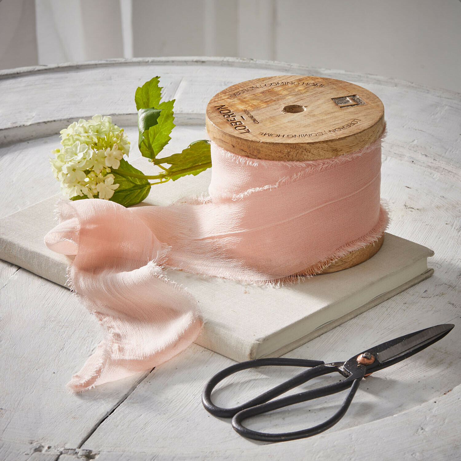Band Lunebrook Rosa Stoffband auf Holzspule mit Schere und Blume auf weissem Tisch arrangiert