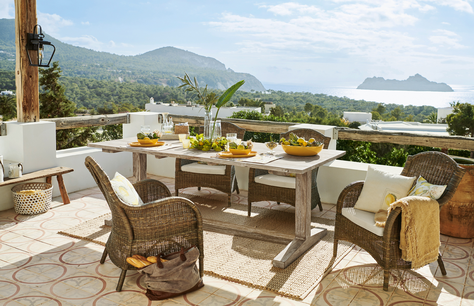 Terrasse mit Rattanmöbeln und hellem Holztisch mit Meeres- und Bergsicht im mediterranen Stil