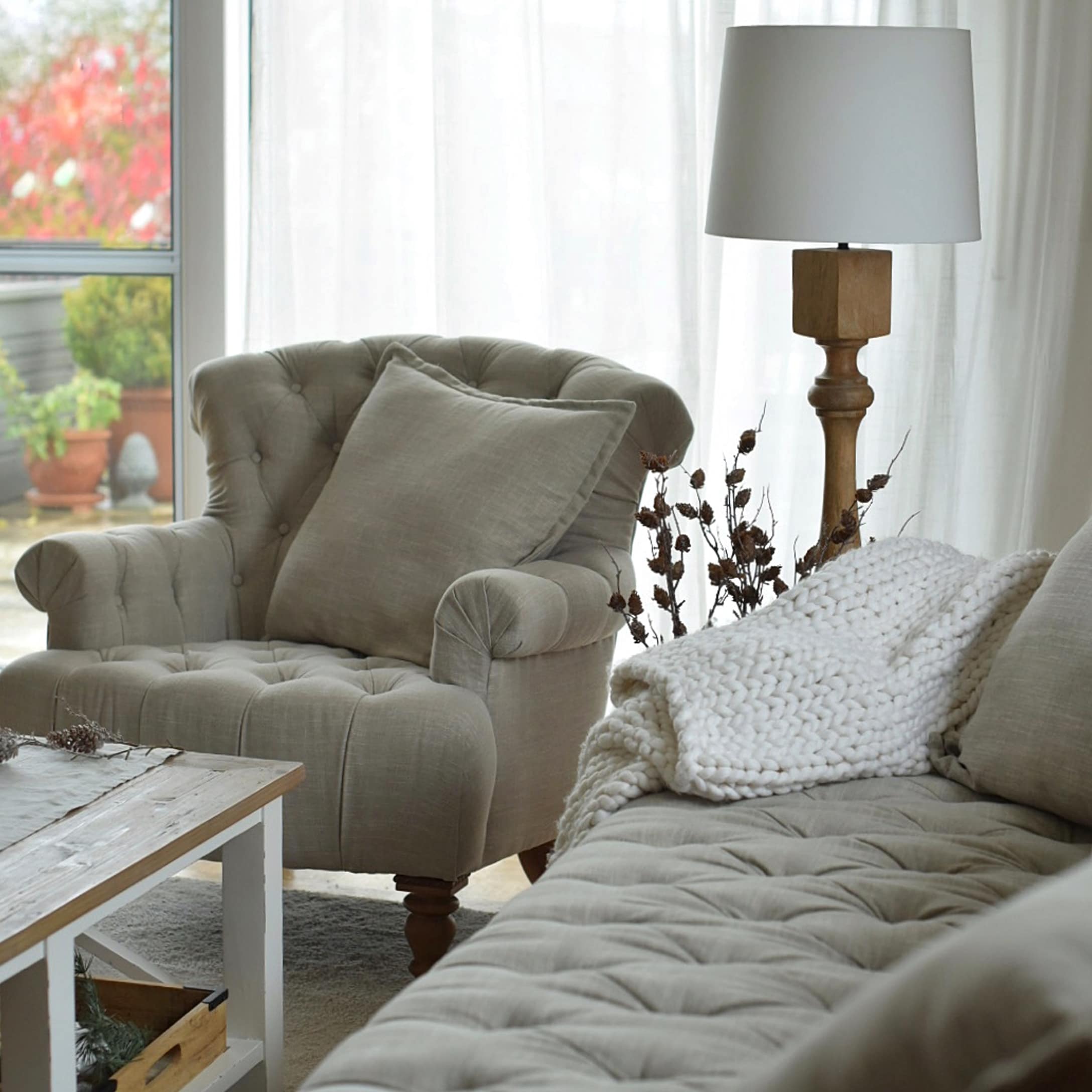 Beiger gepolsterter Sessel und Sofa mit Kissen und weisser Strickdecke in gemütlichem Wohnzimmer