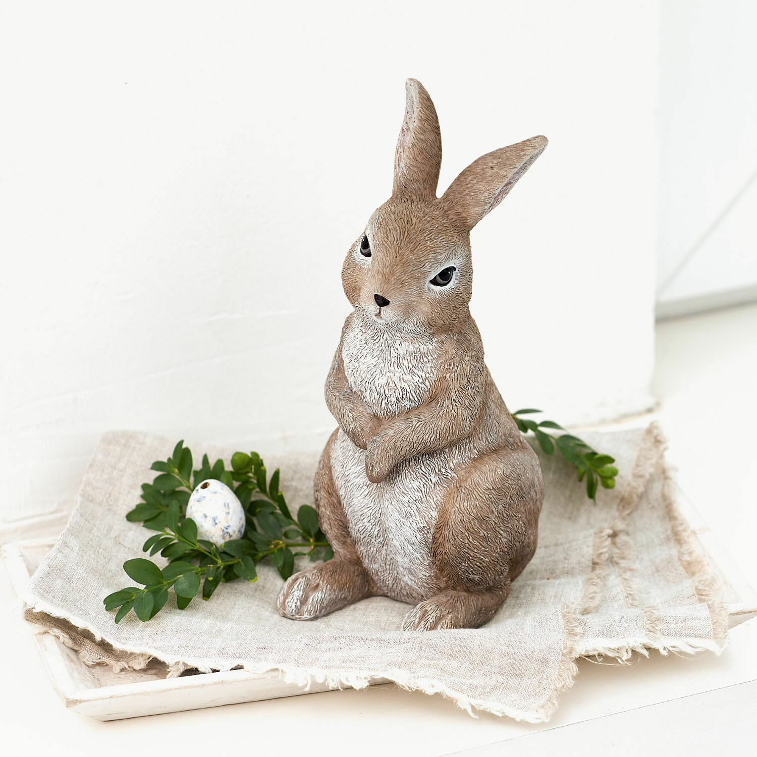 Deko-Hase Milli Dekorative braun-weisse Hasenfigur aus Kunststein auf Leinenstoff mit grünen Blättern und Ei