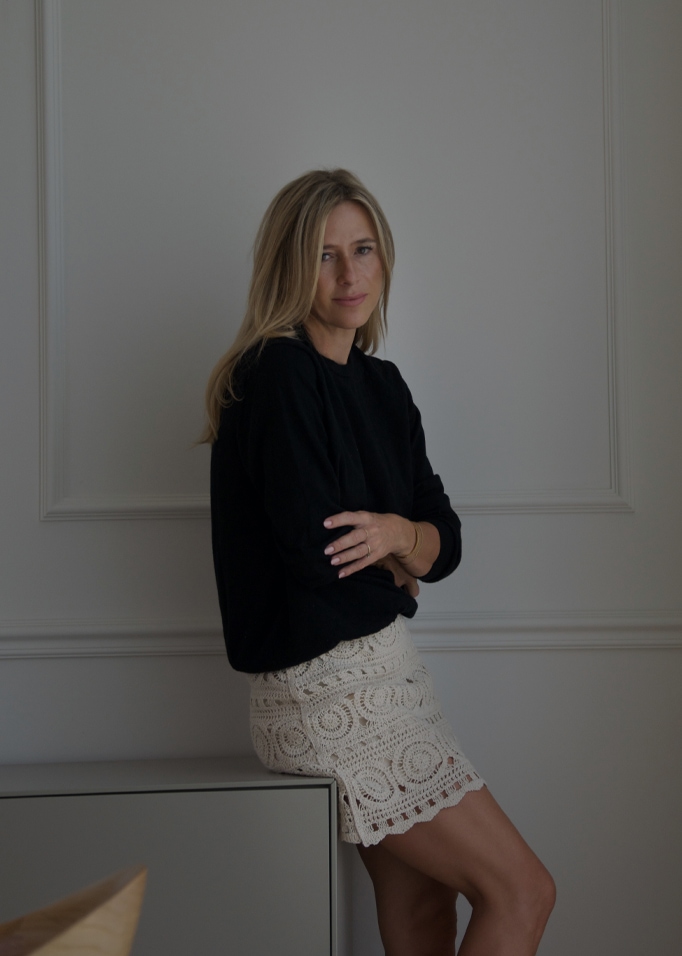 Frau in schwarzem Pullover und cremefarbenem Spitzenrock vor hellem Wandhintergrund, Damenmode