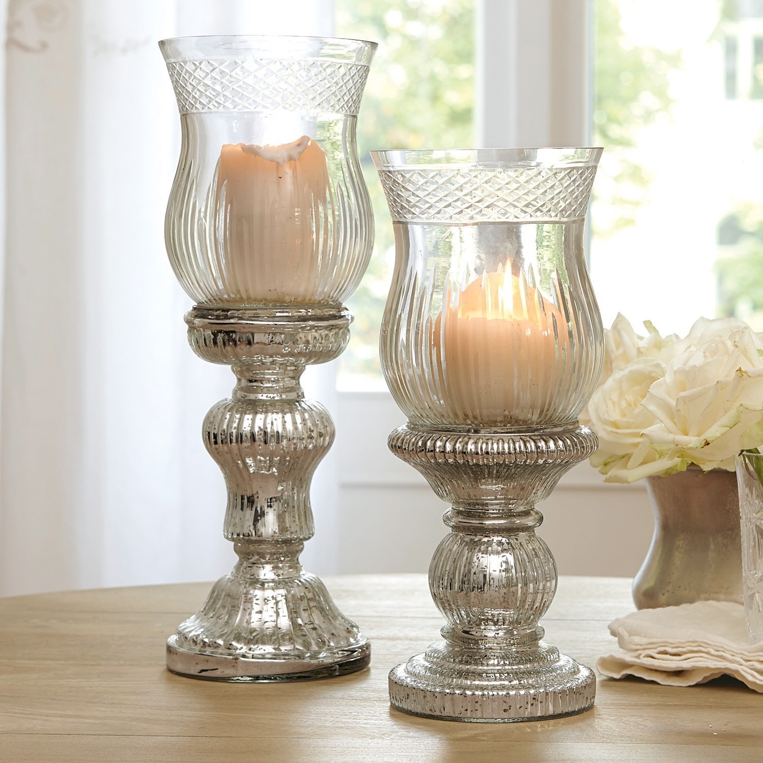 Zwei dekorative Kerzenhalter aus Glas mit antiksilbernem Effekt auf Holztisch in hellem Raum