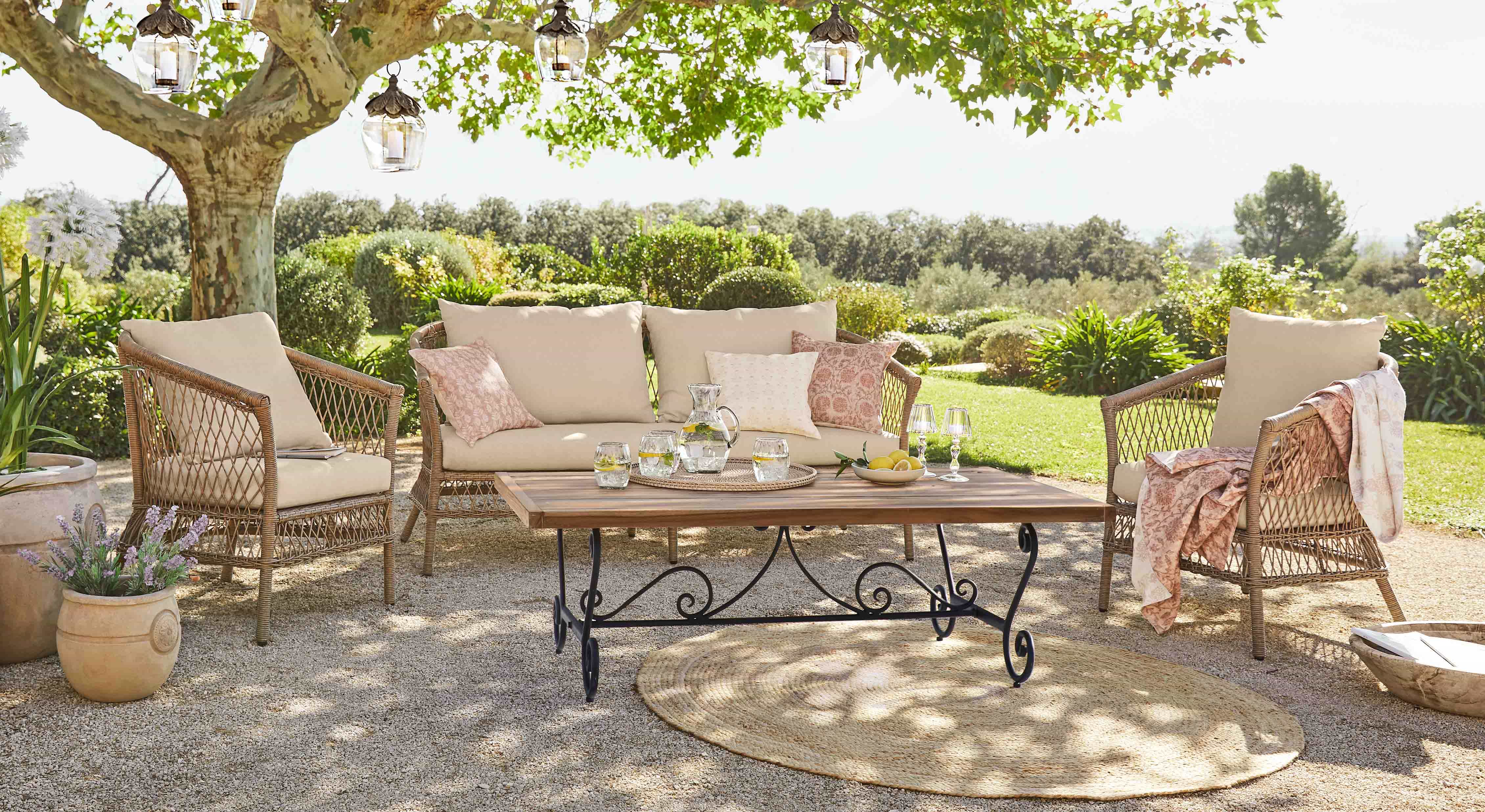 Gartenmöbel-Set aus Rattan mit beigen Polstern und Holztisch auf sonniger Terrasse im Garten