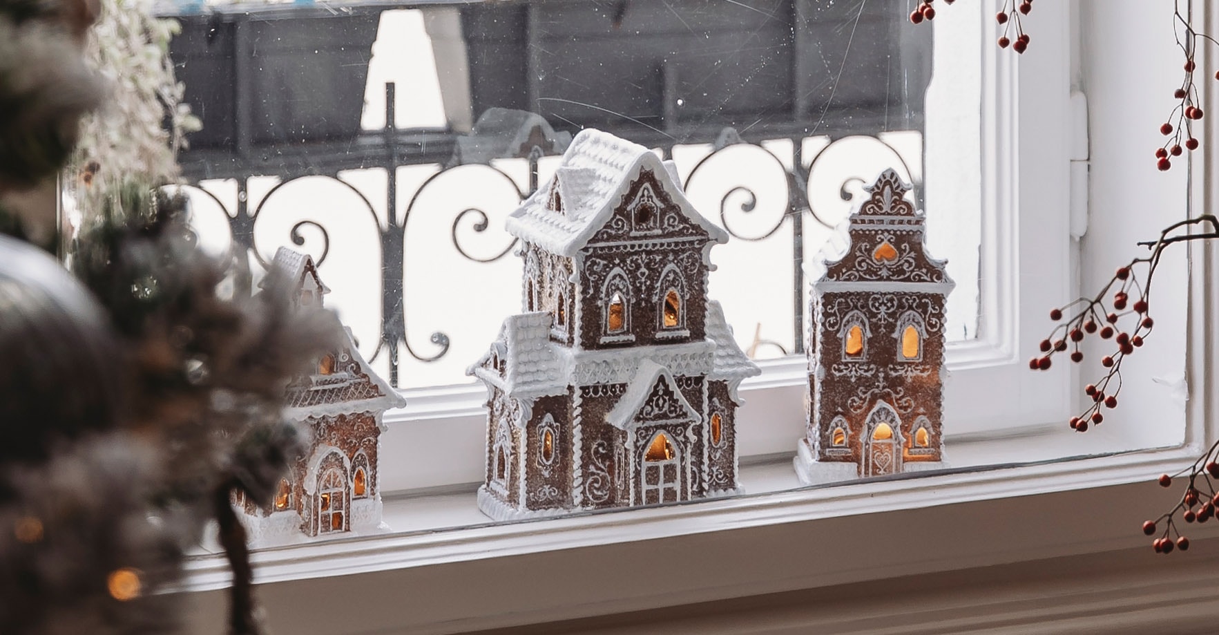 Dekorative Lebkuchenhäuser mit weisser Glasur und Beleuchtung auf dem Fensterbrett zur Weihnachtszeit