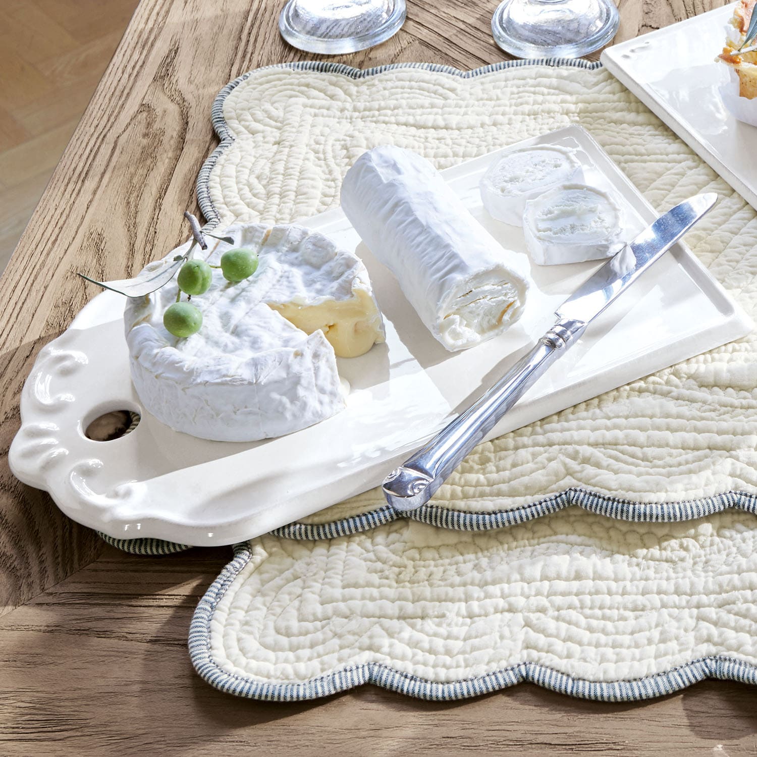 Keramikplatte mit weissem Ziegenkäse und Messer auf gesteppter cremefarbener Unterlage auf Holztisch