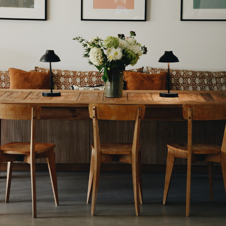 Holztisch mit drei Stühlen, schwarzen Lampen und Vase mit weißen Blumen in gemütlichem Wohnzimmer