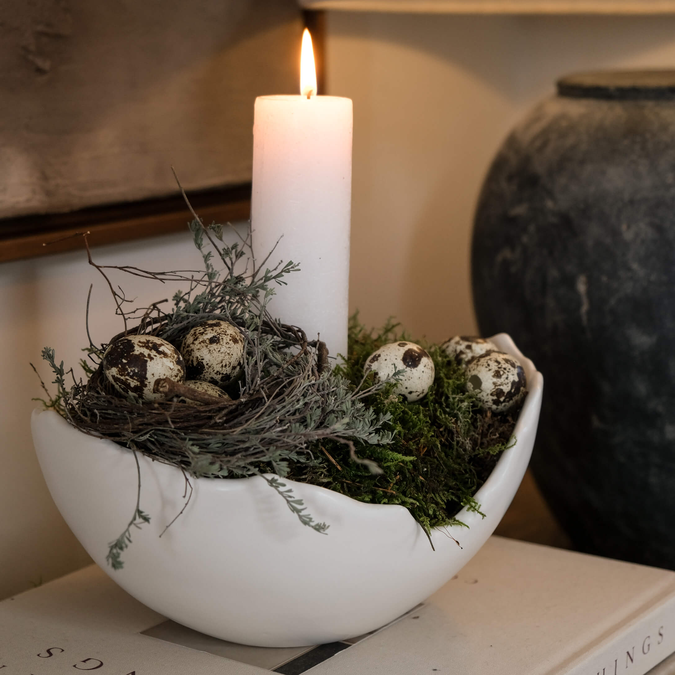 Weisse Keramikschale mit Moos, Nest und brennender Kerze als natürliche Tischdekoration