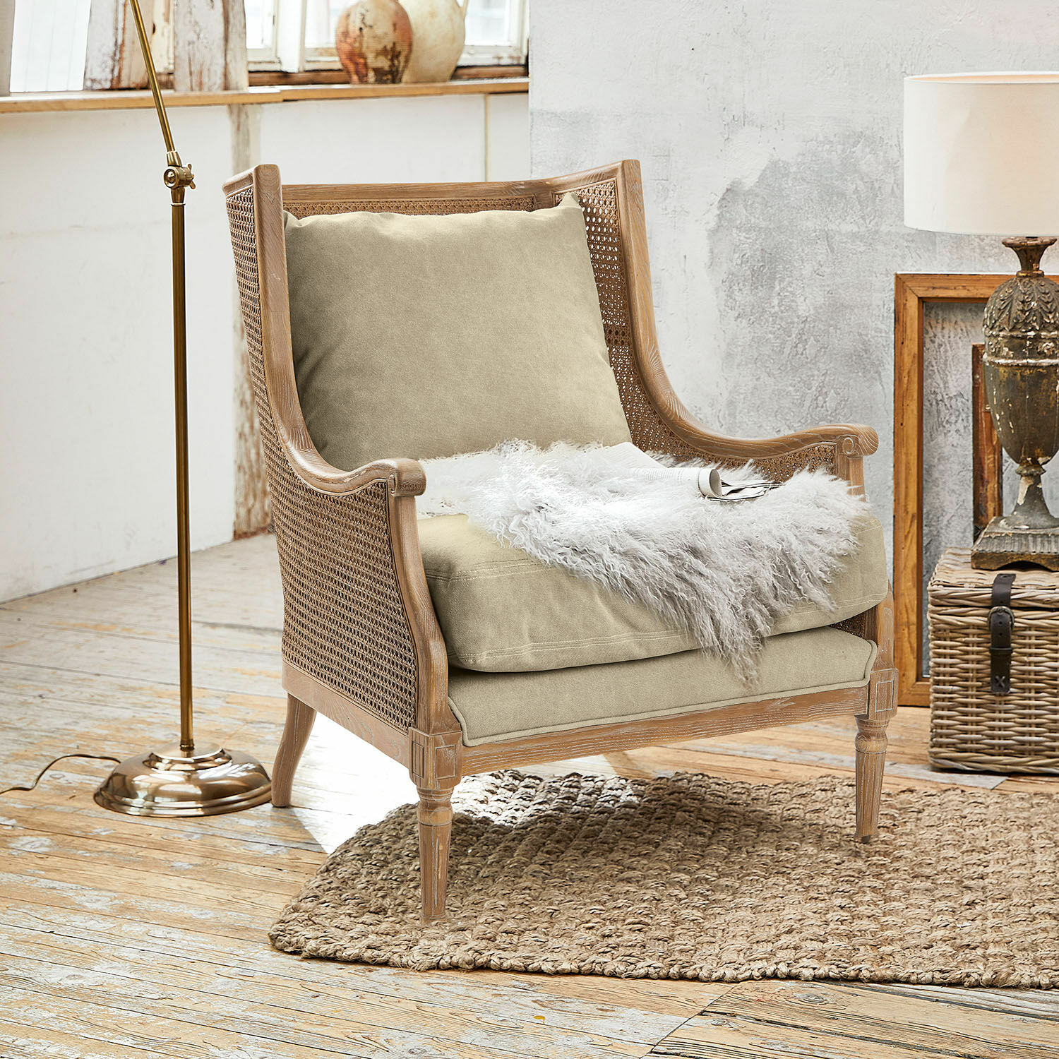 Sessel Greenbrier Sessel aus Holz und Rattan mit beigem Kissen und weissem Fellplaid auf Naturteppich im Raum