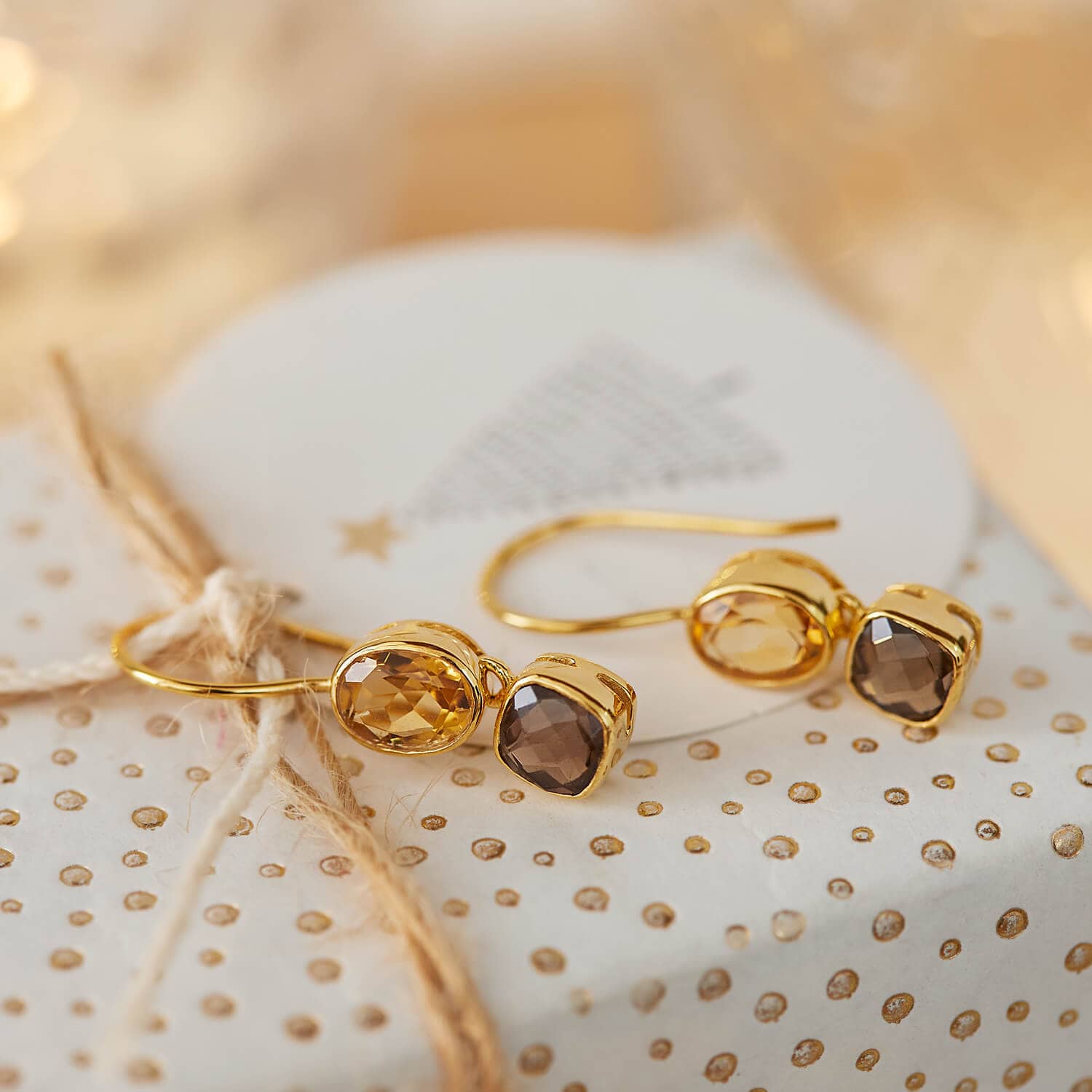 Goldene Ohrringe mit facettierten braunen und bernsteinfarbenen Steinen auf festlichem Hintergrund