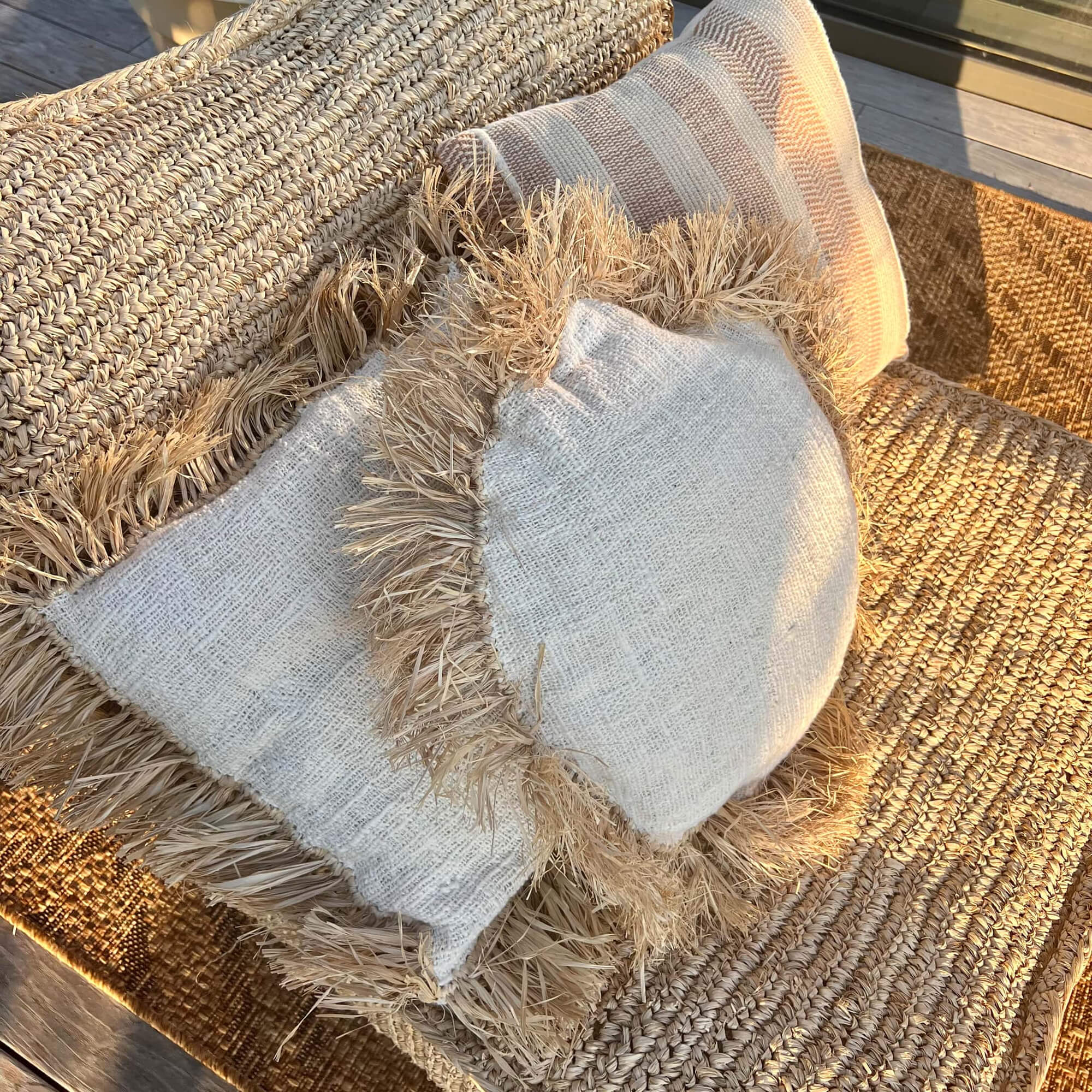 Natürliche Dekokissen mit Fransen auf beigem geflochtenem Sitz, Boho-Stil und gemütliche Atmosphäre