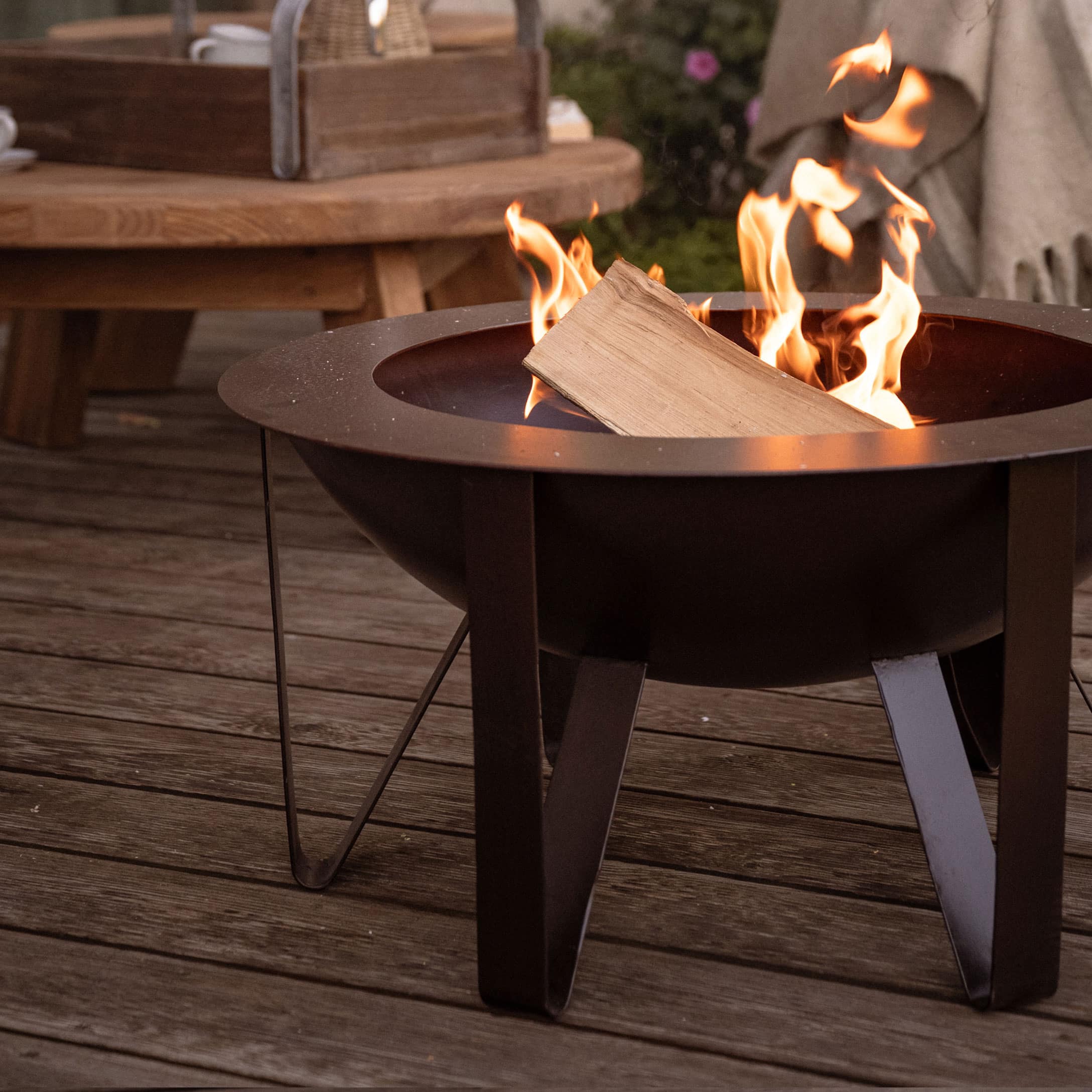 Schwarzer Metall-Feuerkorb mit brennendem Holz auf Holzterrasse für gemütliche Abende