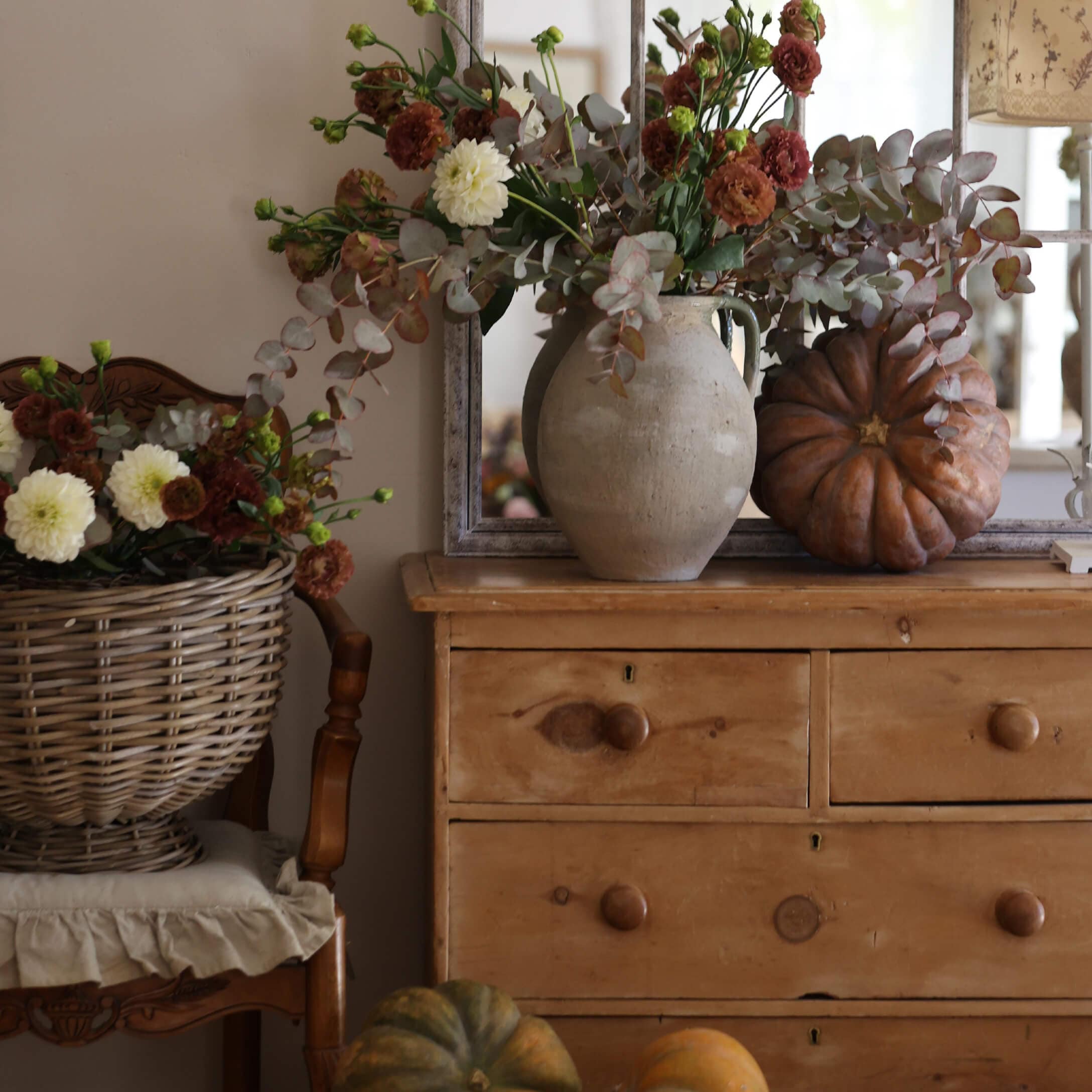 Rustikale Holzkommode mit Tonvase, herbstlichem Blumenstrauss und dekorativen Kürbissen in gemütlicher Umgebung