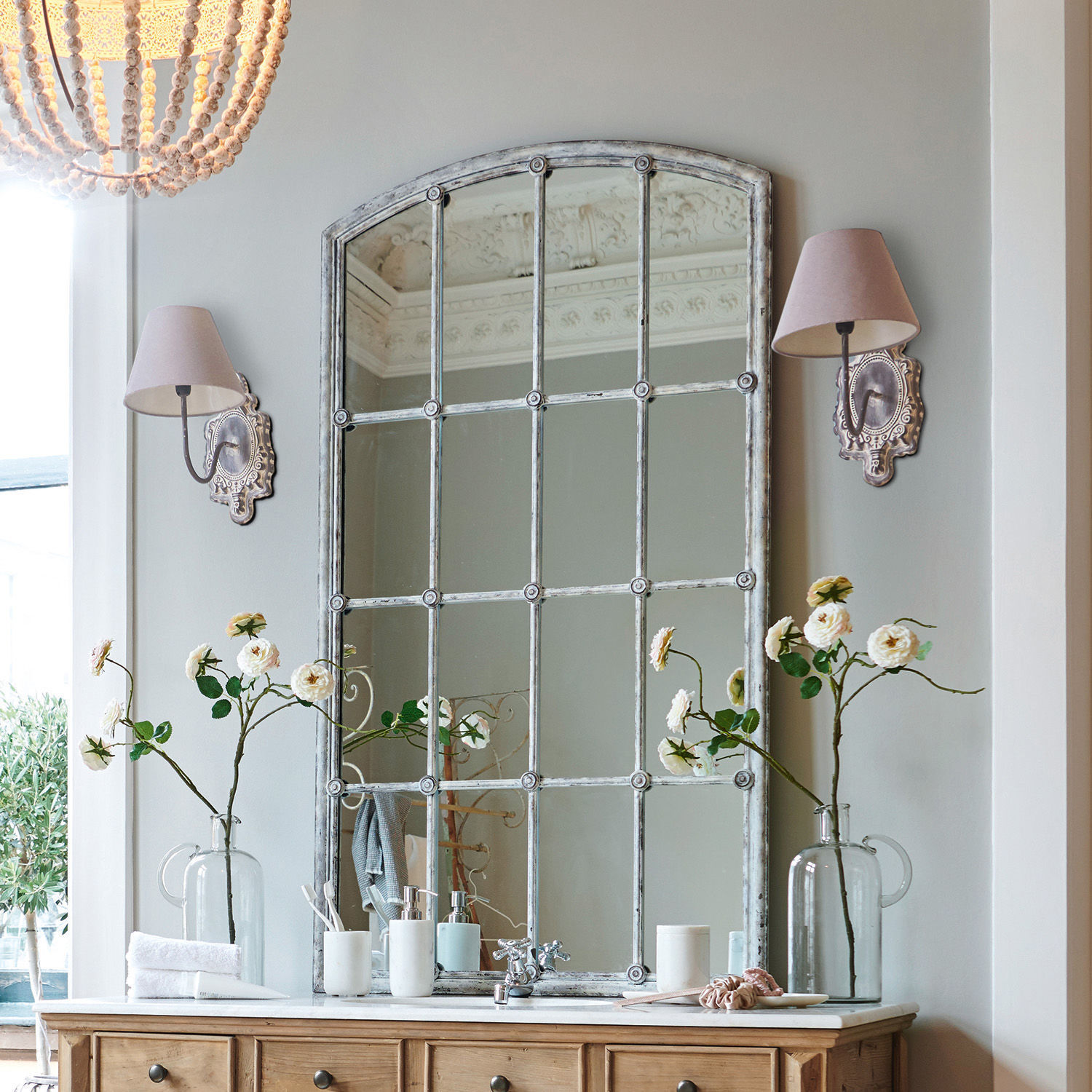 Spiegel Tobiah Grosser Vintage-Spiegel mit Metallrahmen über Holzkommode mit Blumen und Wandlampen im Badezimmer