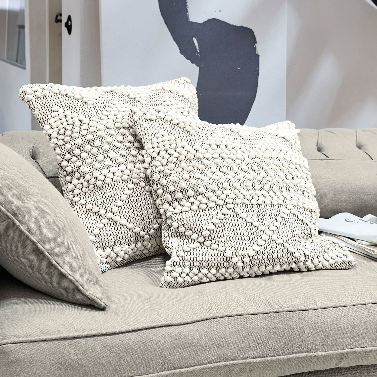 Kissenhülle 2er Set Hadir Zwei cremefarbene Baumwollkissen mit Struktur und geometrischem Muster auf grauem Sofa