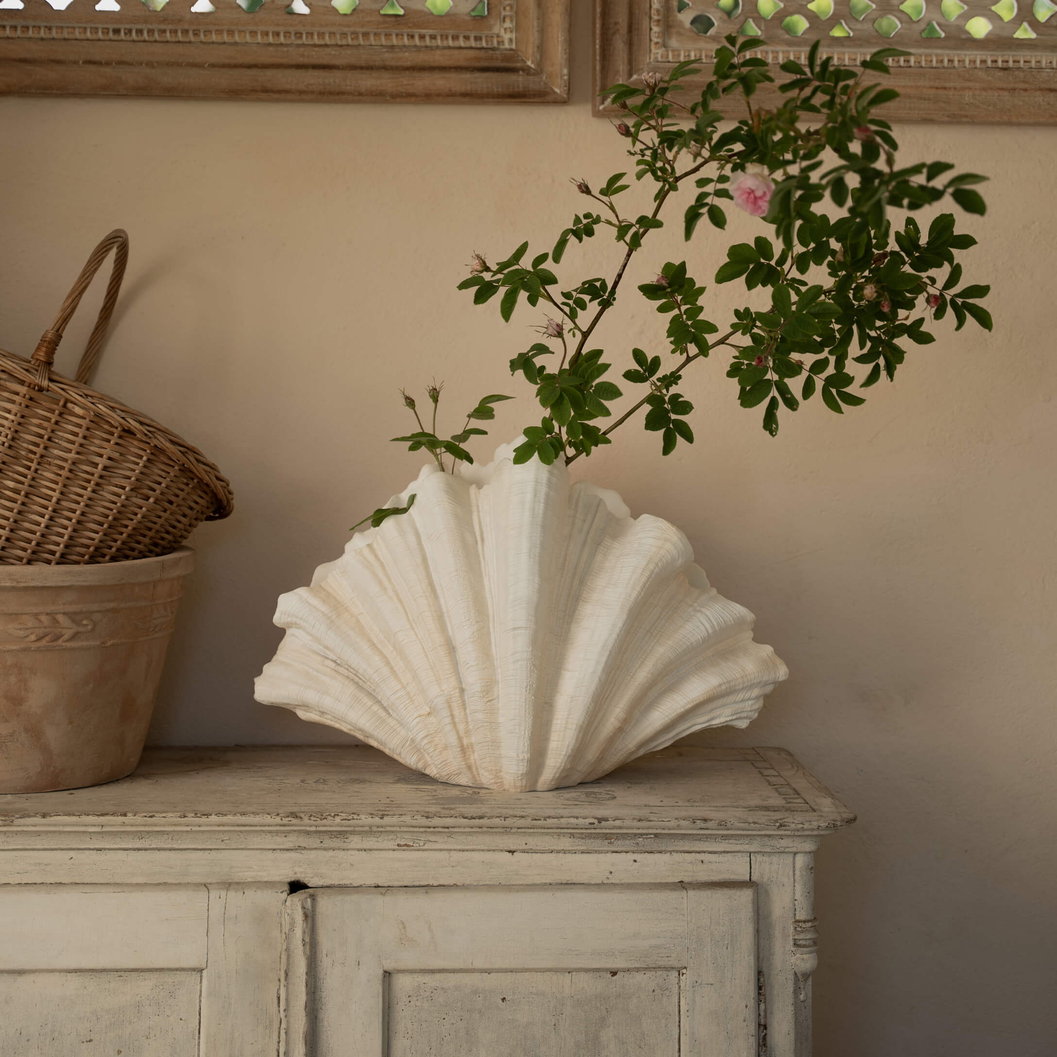 Weisse Keramikvase in Muschelform mit grünen Zweigen auf einem antiken Holzschrank