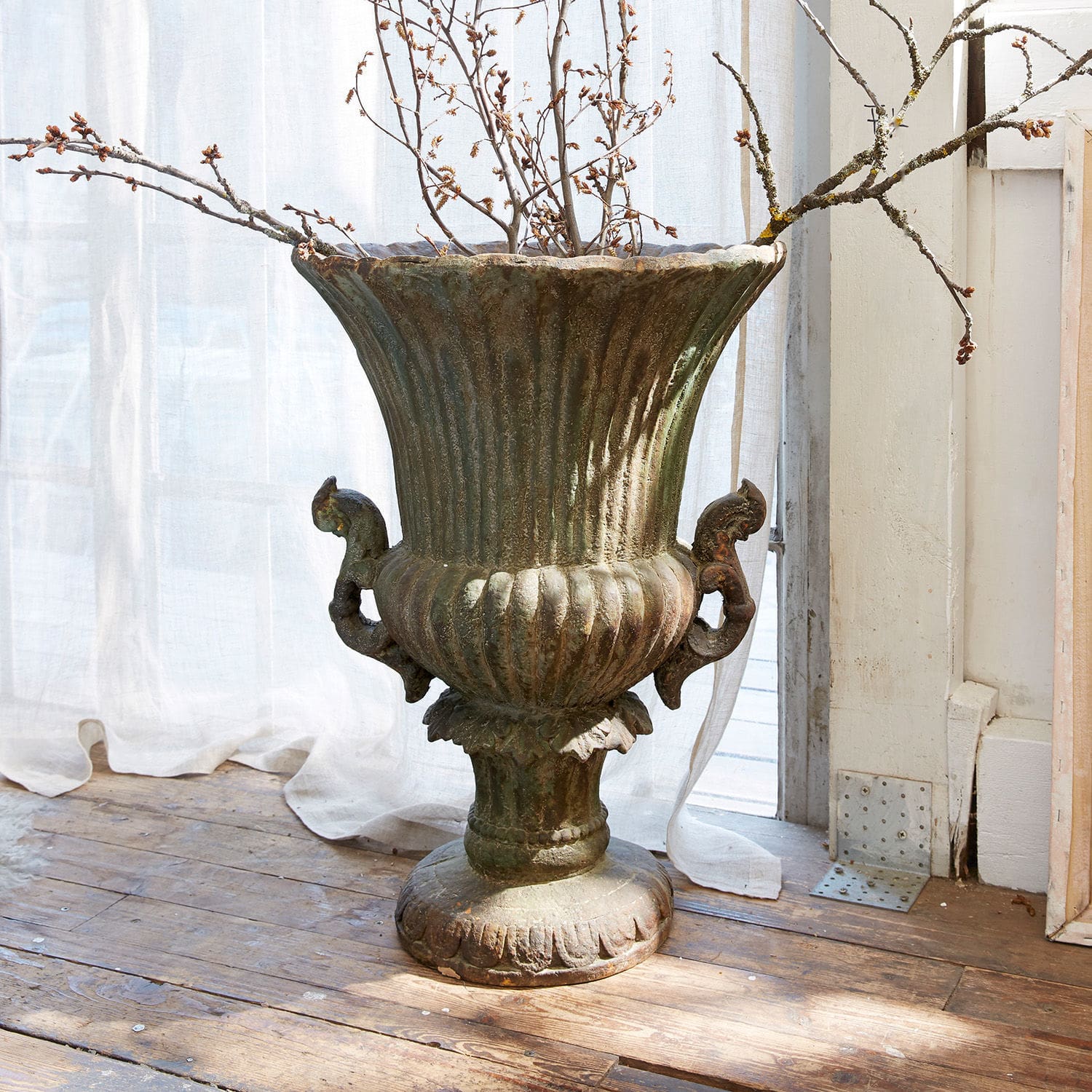 Amphore Estefanie Grosse dekorative Vase aus Metall in patinierter Grünton auf Holzboden mit Zweigen