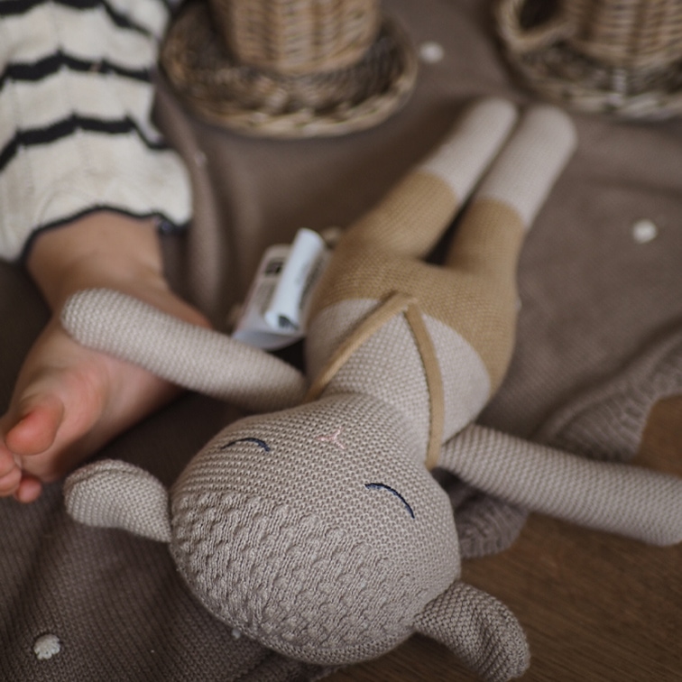 Weiches gestricktes Kuscheltier in Beige- und Brauntönen auf braunem Hintergrund