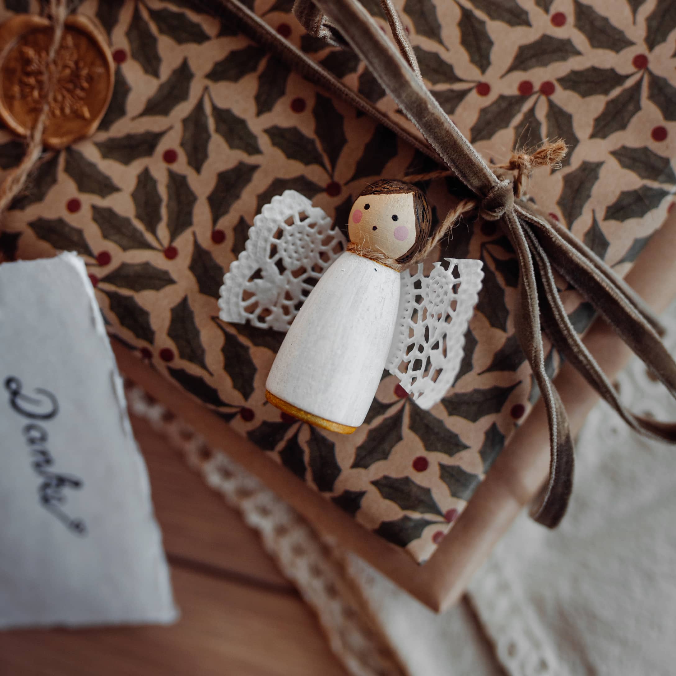 Holzengel mit weissen Spitzenflügeln auf Geschenk mit gemustertem Papier und Samtschleife