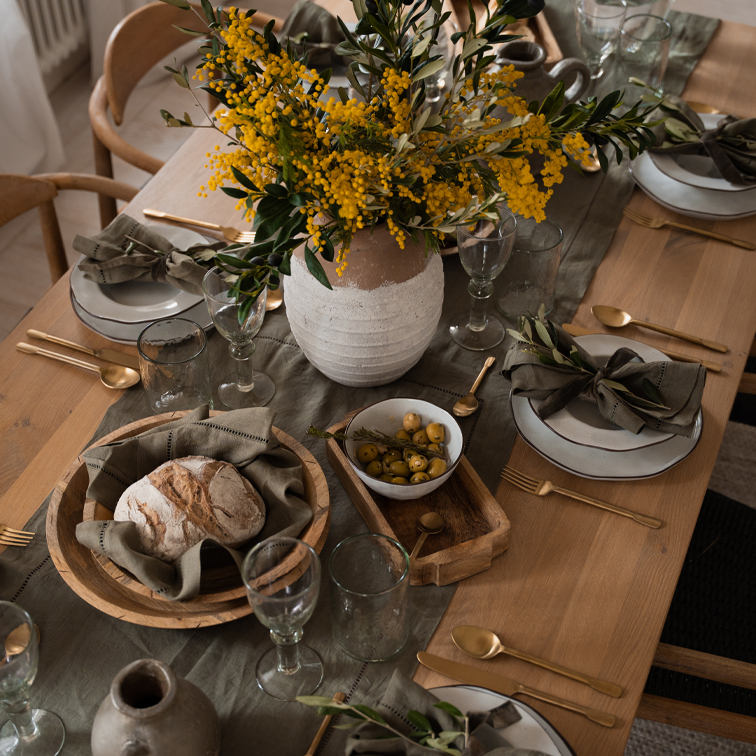 Rustikaler Holztisch mit weissen Keramiktellern, Holzschalen und gelben Blumen in Tonvase