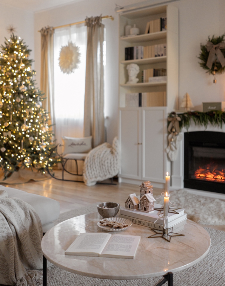Gemütliches Wohnzimmer mit hellem Marmortisch, beleuchtetem Weihnachtsbaum und brennendem Cheminée