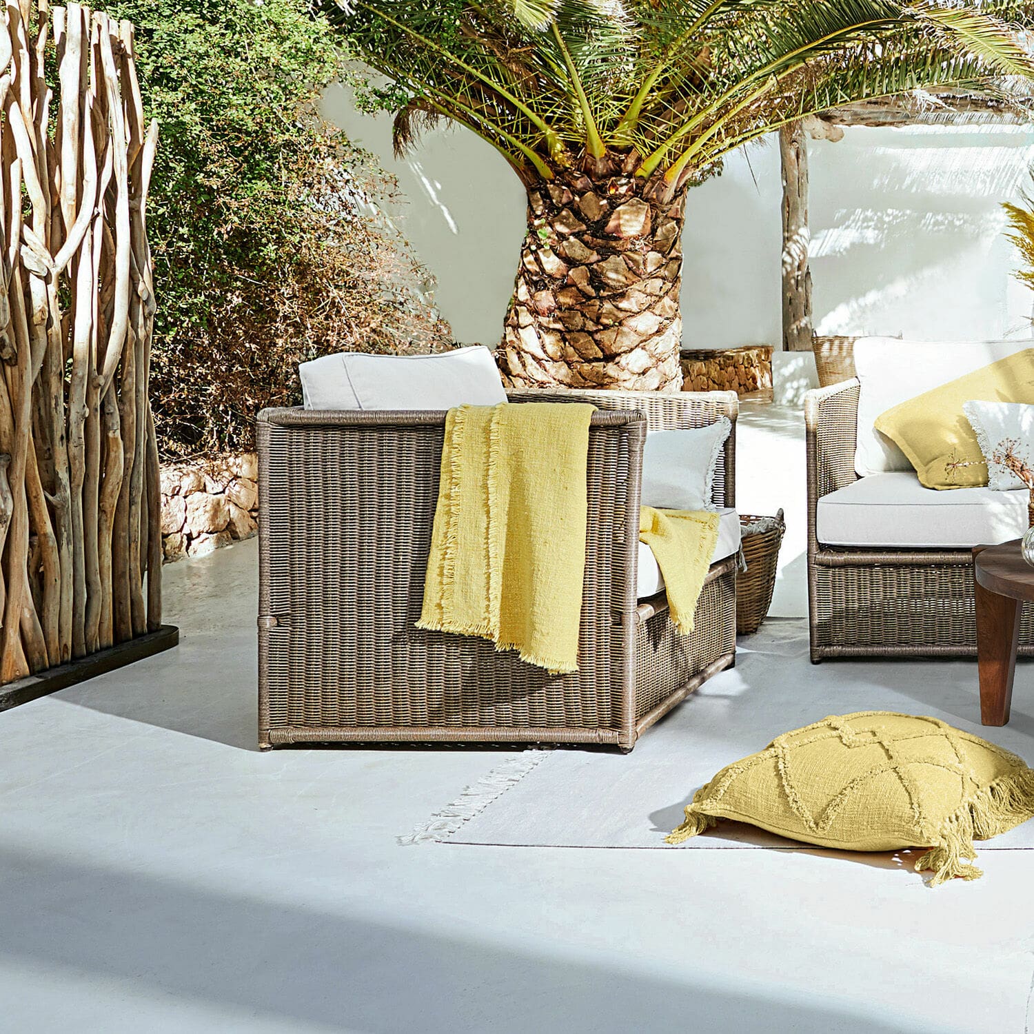 Sessel Lesmont Braunes Rattan-Gartenmöbel-Set mit weissen Kissen und gelben Akzenten auf sonniger Terrasse
