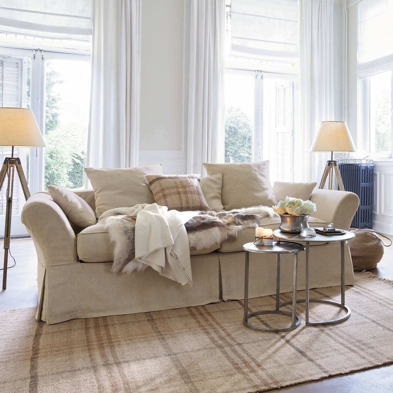 Sofa Worcester Beiges Stoffsofa mit Kissen und Fell-Decke auf hellem Teppich in hellem Wohnzimmer mit Stehlampen