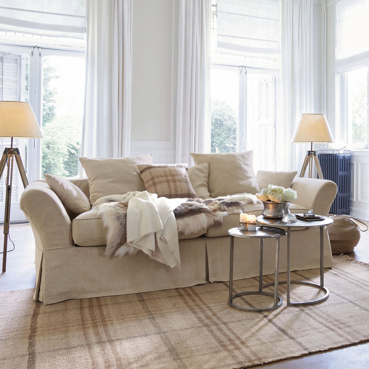 Sofa Worcester Beiges Stoffsofa mit Kissen und Fell-Decke auf hellem Teppich in hellem Wohnzimmer mit Stehlampen