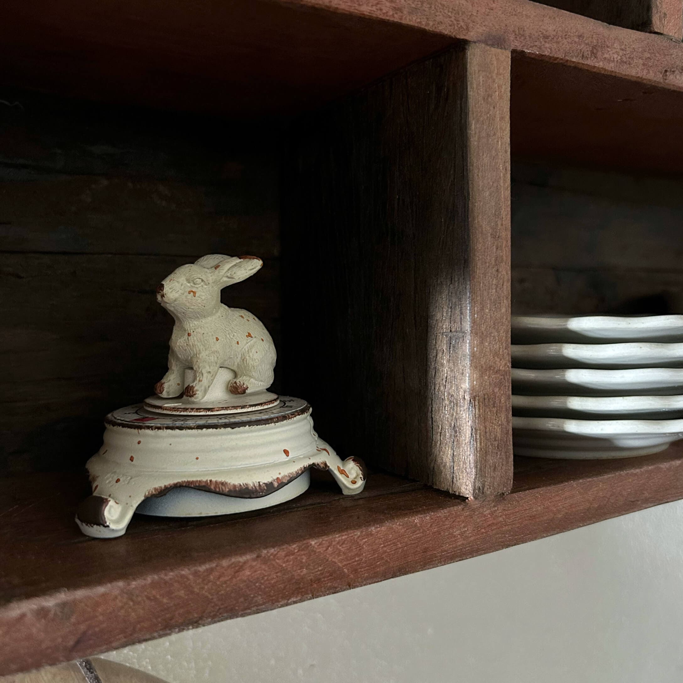 Weisser Keramikbehälter mit Hasenfigur als Deckel auf Holzregal neben Tellern