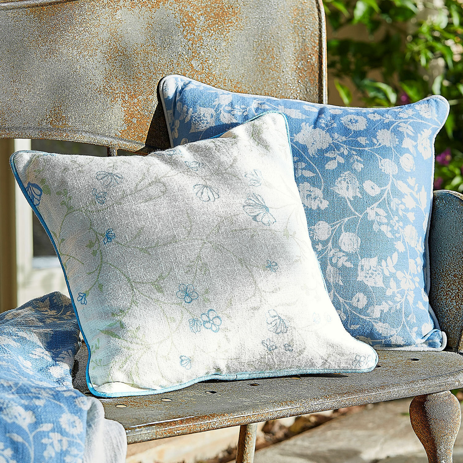 Kissenhülle 2er Set Corvelique Zwei dekorative Baumwollkissen in Blau-Weiss mit Blumenmuster auf rostiger Metallbank im Garten