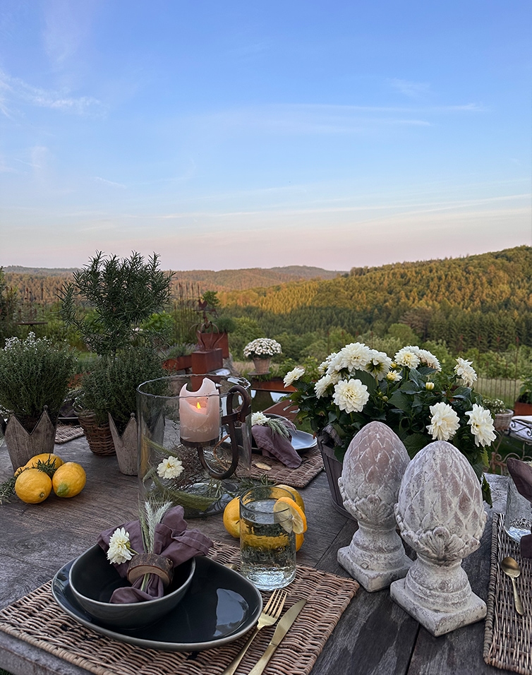 Rustikaler Tisch mit Steindekorationen und weissen Blumen vor grünen Hügeln und blauem Himmel
