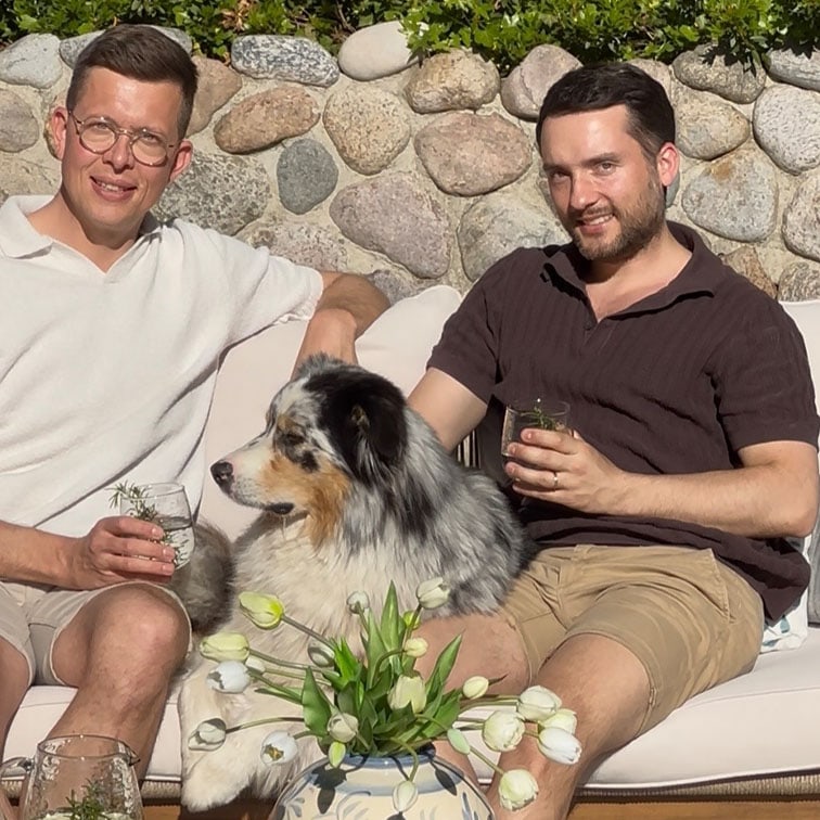 Zwei Männer sitzen draussen auf einer Couch mit einem Australian Shepherd und weissen Tulpen im Vordergrund.