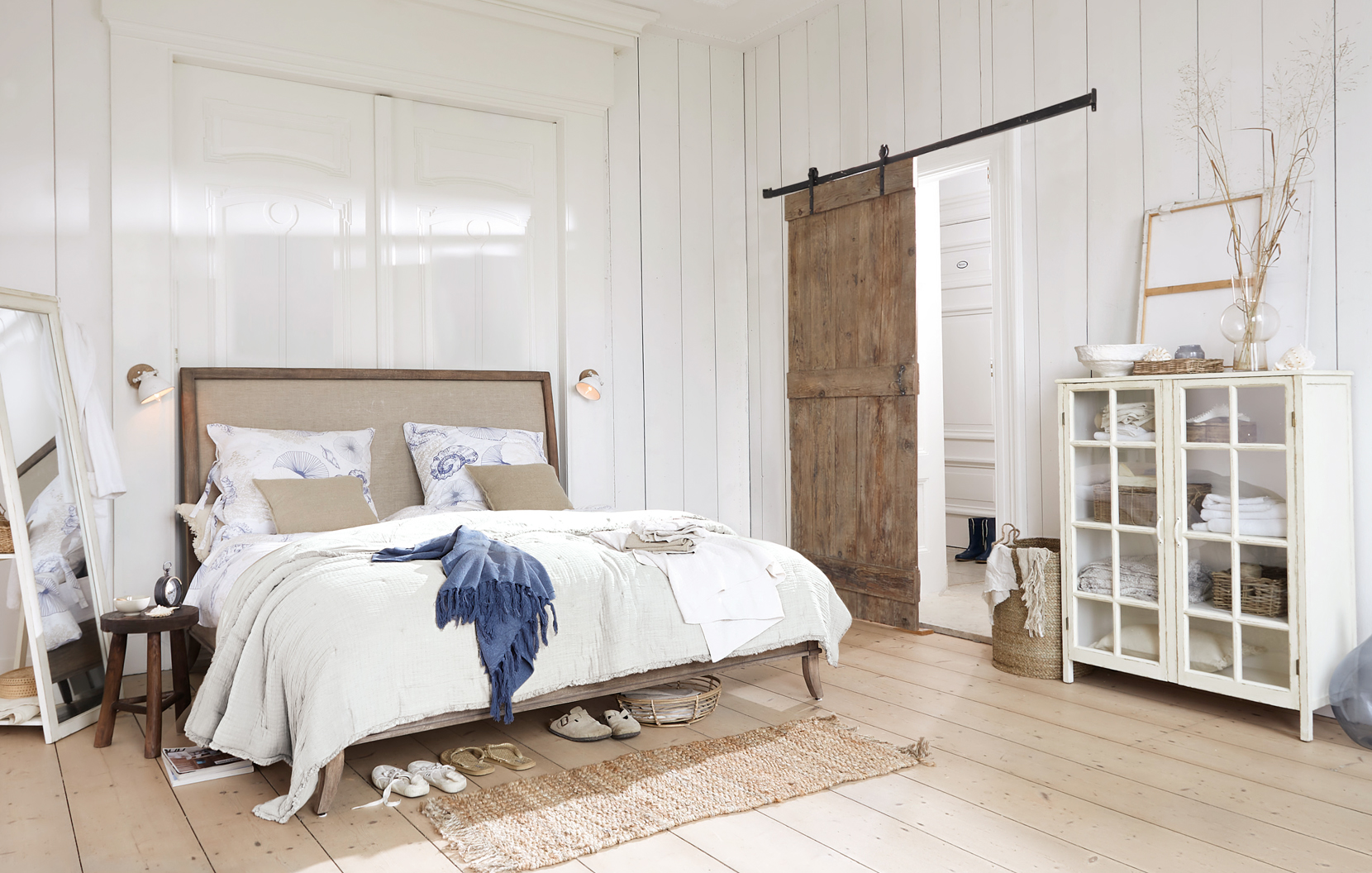 Helle Schlafzimmer mit Holzbett, weisser Bettwäsche und rustikalem Glas-Holz-Kleiderschrank