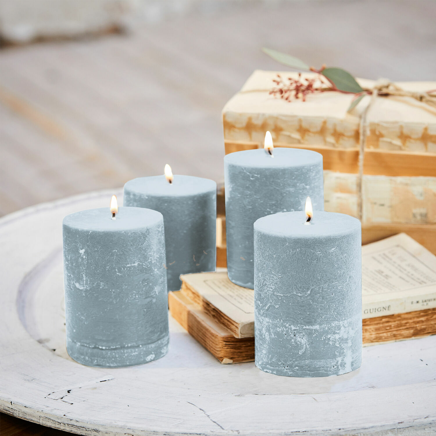 Kerze 4er Set Virrans Set aus vier blauen Wachskerzen auf weissem Holztisch mit Büchern und Geschenkbox