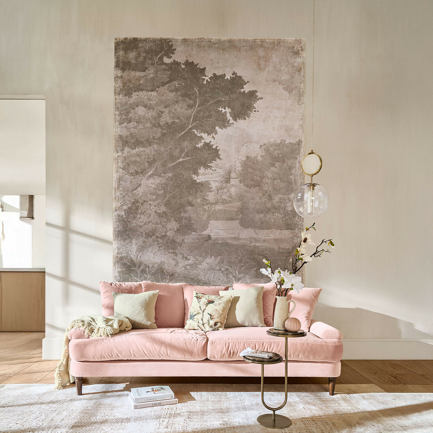 Rosa Samtsofa mit Kissen und Beistelltisch mit Blumen in hellem Wohnzimmer mit Wanddekoration