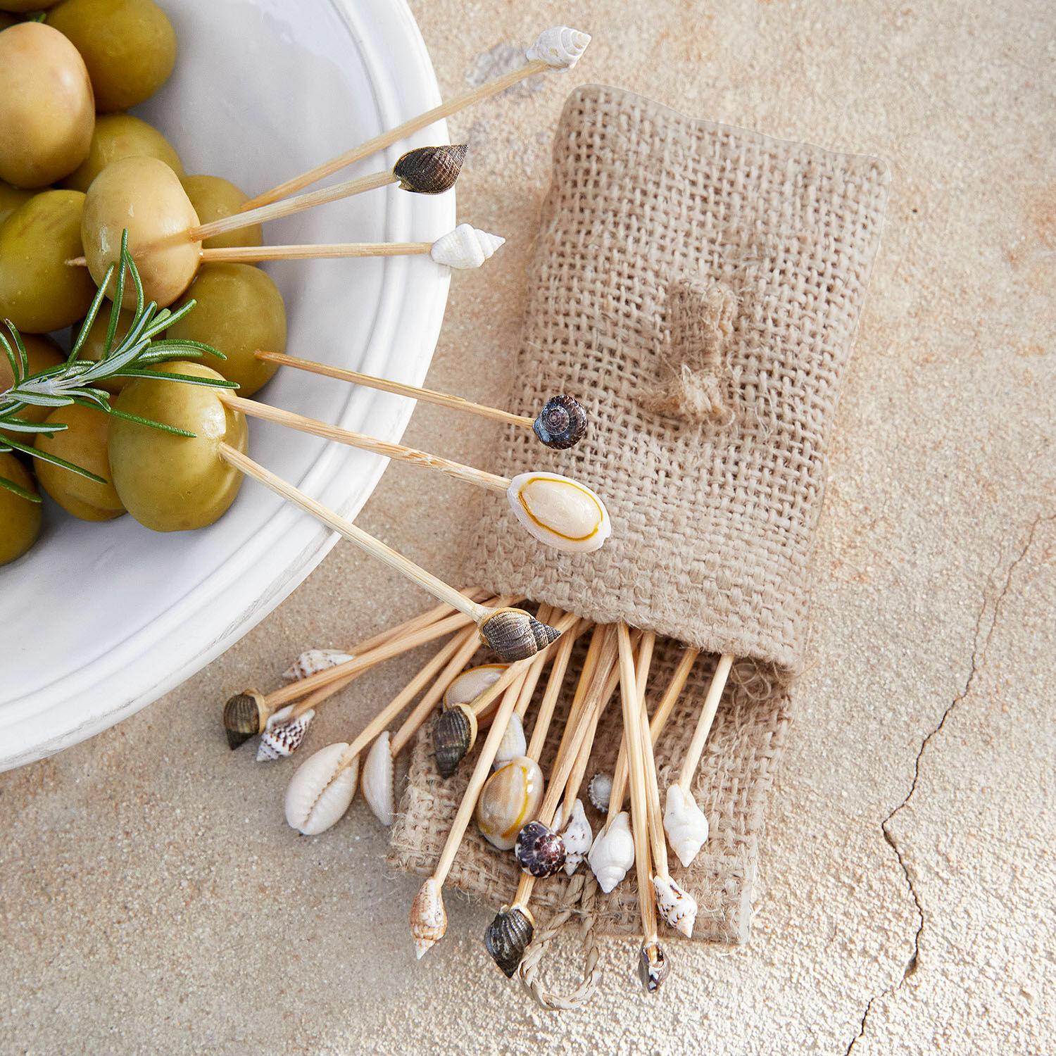 Muschelsticker Bijou Set aus Holzspiessen mit natürlichen Muscheln im Jutebeutel neben grünen Oliven