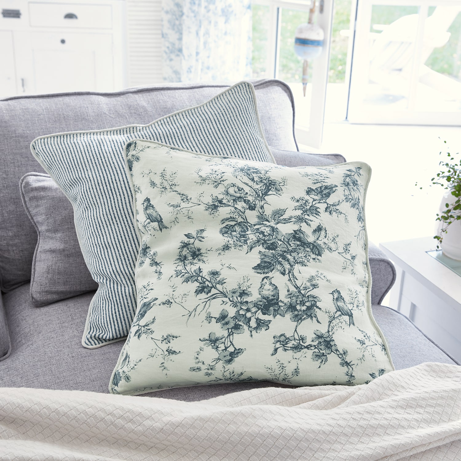 Wendekissen aus Baumwolle mit blauen Blumen- und Streifenmustern auf grauem Sofa