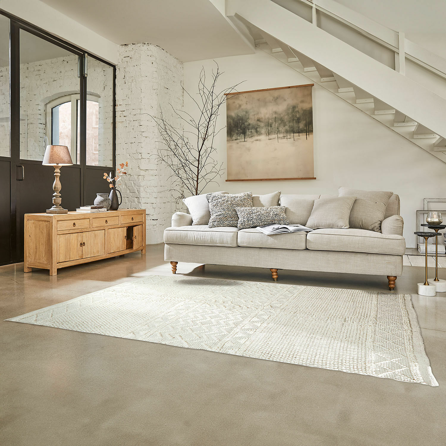 Teppich Hadir Beiges Sofa mit Kissen und helles Holz-Sideboard im hellen Wohnzimmer mit Teppich und Wandbild