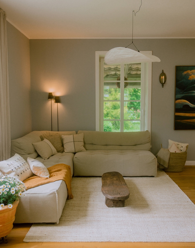 Gemütliches Wohnzimmer mit beigem Ecksofa, rustikalem Holztisch und hellem Teppich im skandinavischen Stil.
