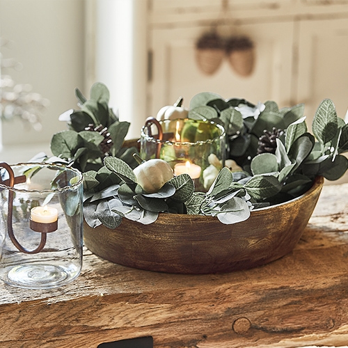 Dekorative Holzschale mit grünen Blättern und Kerze im Glaswindlicht auf Holztisch